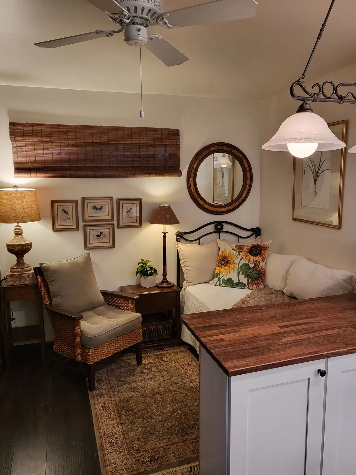 The image showcases a warm, sunlit seating area within the Prescott Rock House Dells Studio Retreat. Cushions, a vibrant sunflower pillow, and soft lamps create a cozy nook, while tasteful décor like a decorative mirror and framed bird illustrations add a touch of charm.