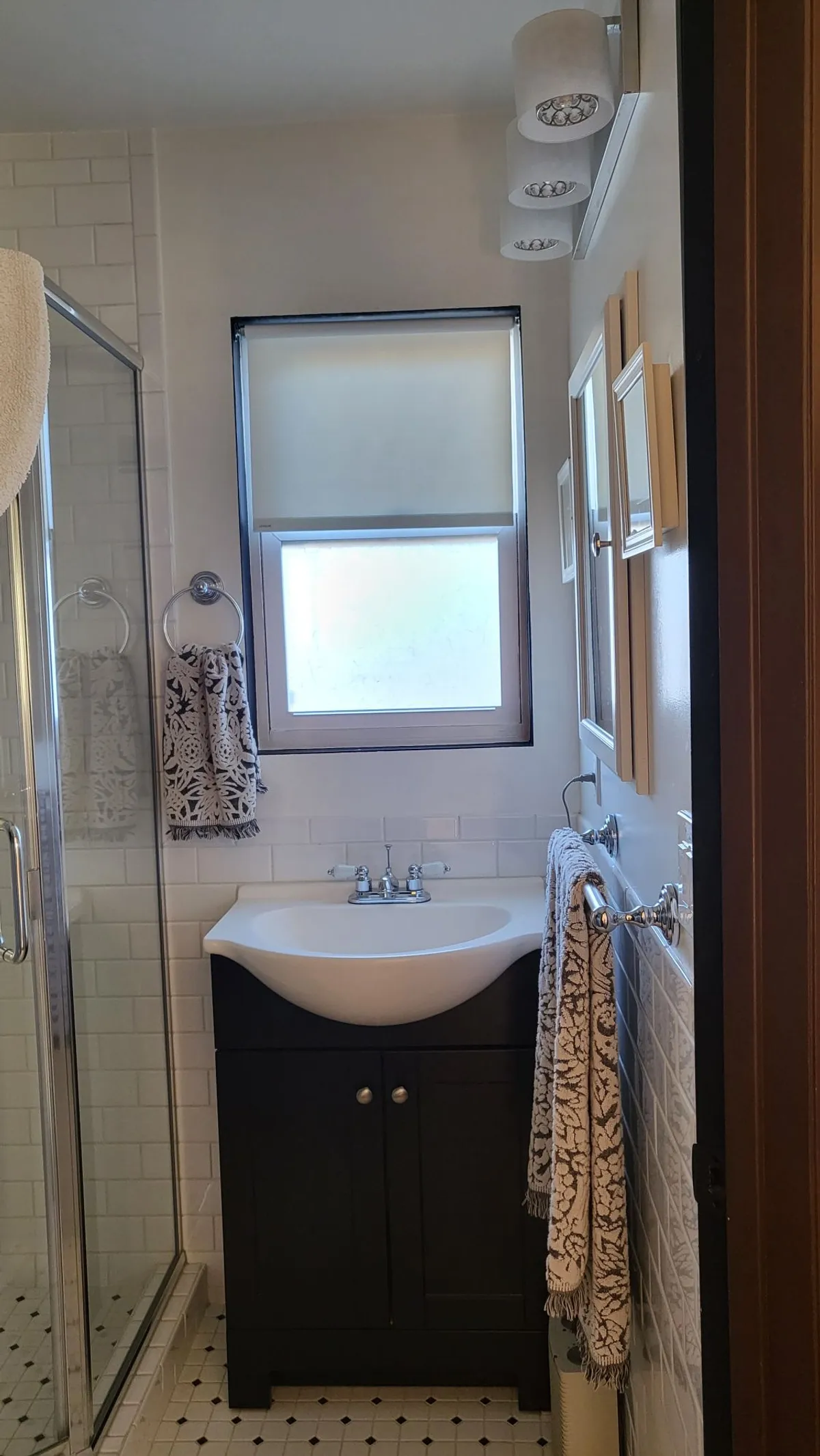 The image displays a well-appointed bathroom with a vanity sink, a walk-in shower enclosure, crisp towels, and decorative framed mirrors. Soft natural light enhances the calm, refreshing mood, suggesting a sanctuary for morning routines or unwinding in the evening.