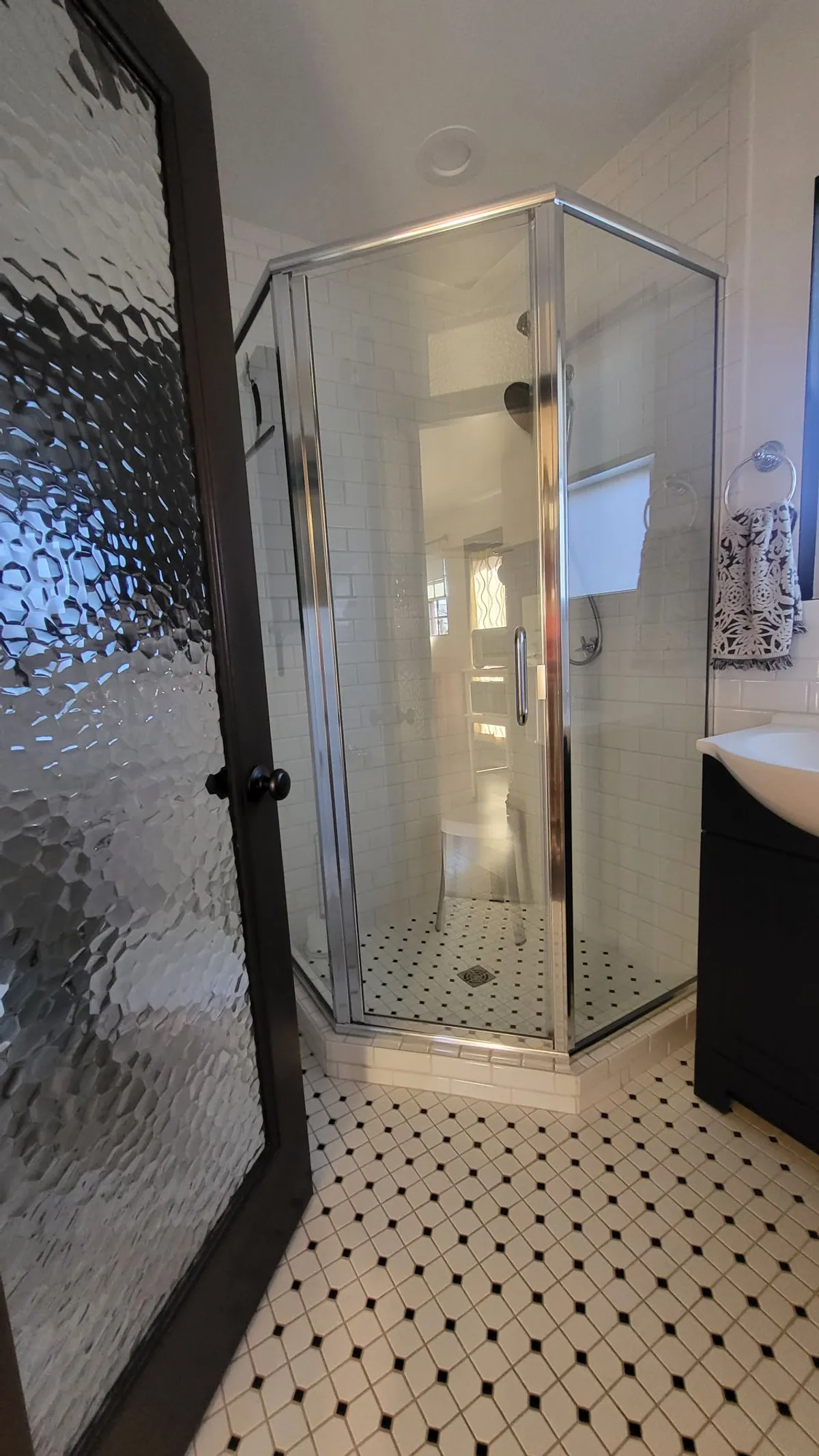 This image highlights a private bathroom featuring a glass shower enclosure, striking black and white tile flooring, and a sleek modern vanity. The clean lines and contemporary fixtures create a calming, spa-like ambiance ideal for relaxing after a day out.