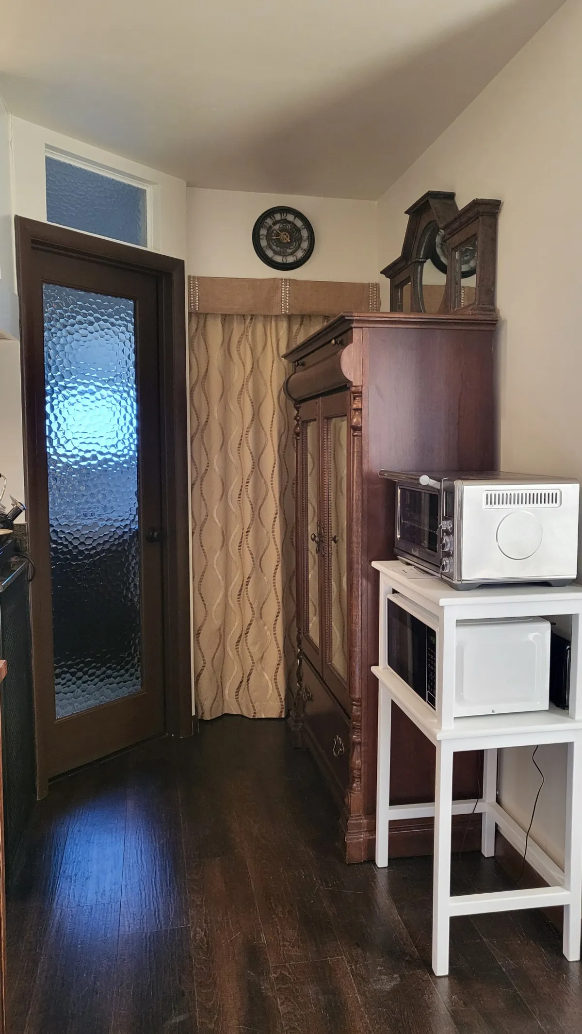 This image features an inviting kitchenette setup with an antique cabinet, a modern microwave, curtains, and a clock. The scene exudes a nostalgic mood, and the focal points lend a sense of warmth and everyday living—perfect for quick meals, coffee breaks, or preparing snacks.