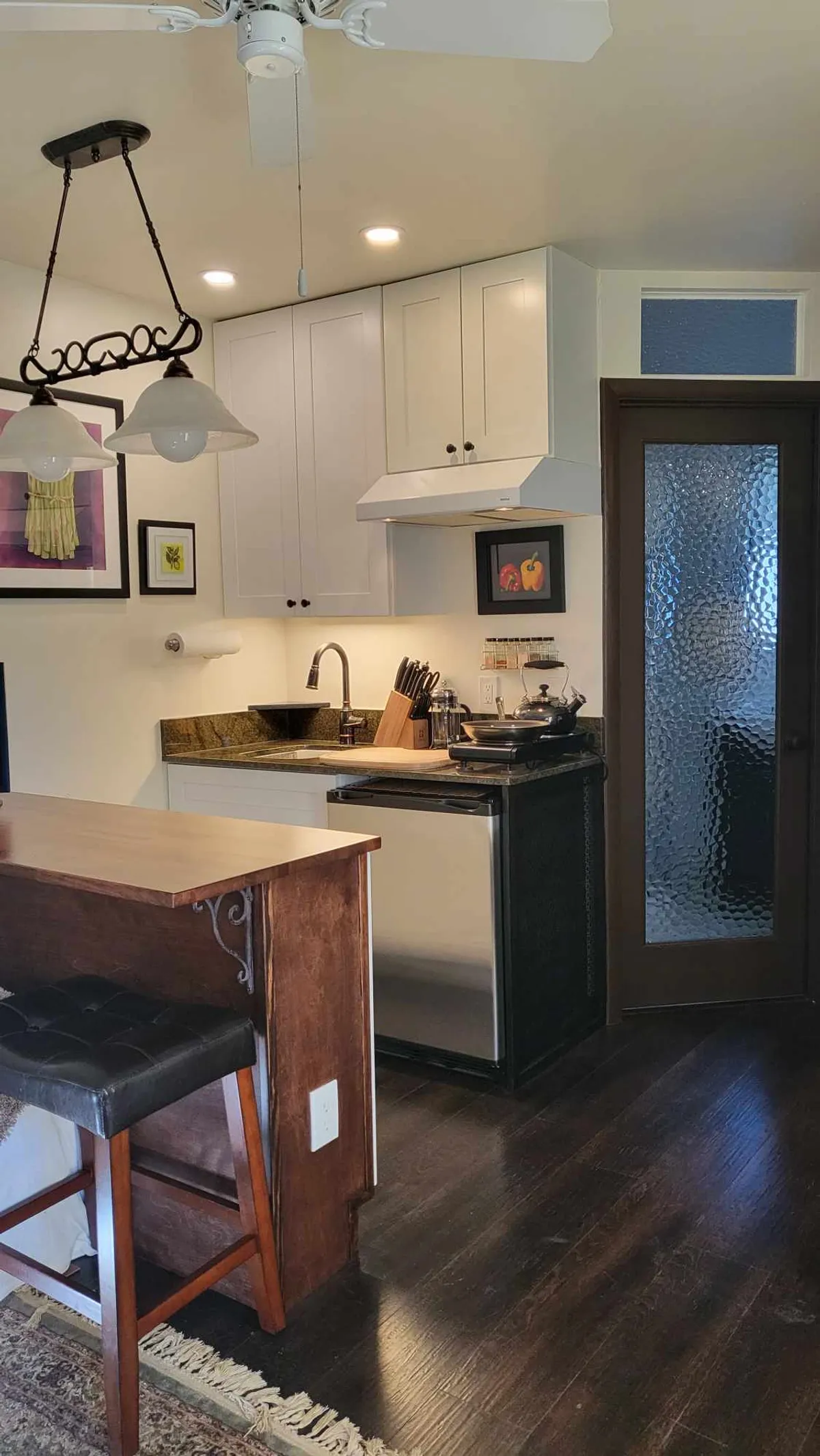 A bright, open-plan kitchen features a central island with comfortable stools, stainless steel appliances, and inviting wall art. The space is bathed in natural light, giving it a warm, welcoming feel. The kitchen flows seamlessly into the surrounding living and dining areas, hinting at a fluid layout ideal for both quiet meals and social gatherings.